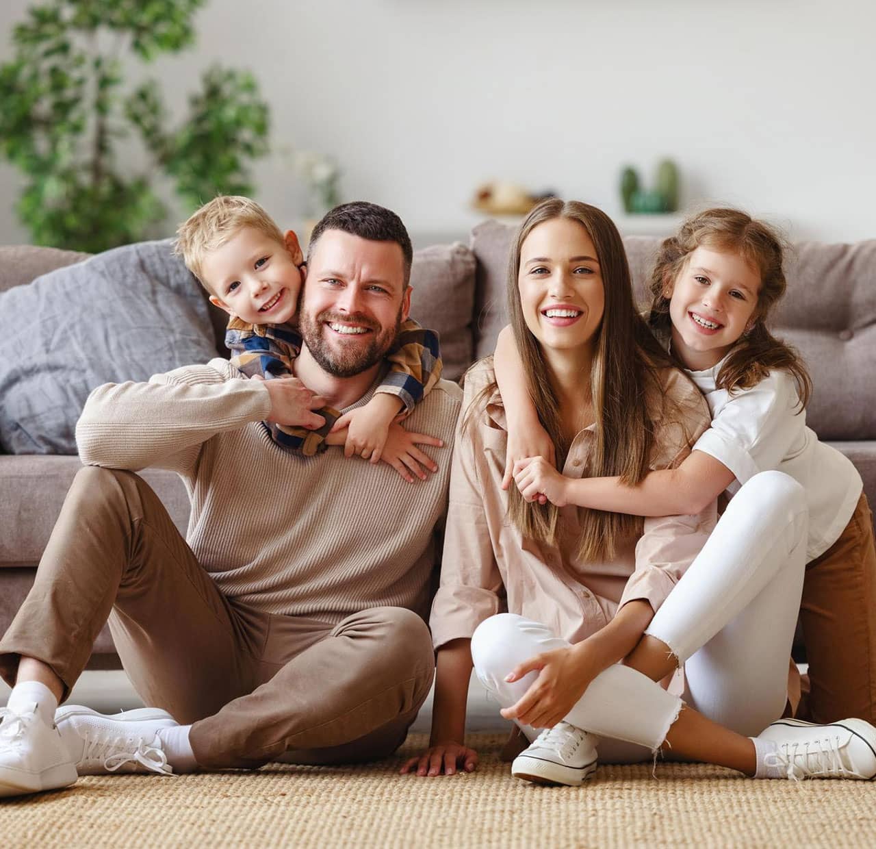 parents with two young kids smiling sitting in front of the couch