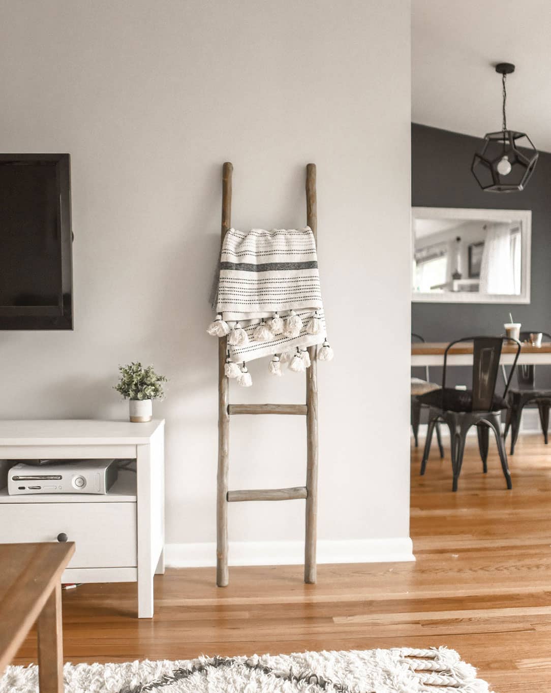 decorative ladder sitting in a modern living room with white walls and the dining room in the background